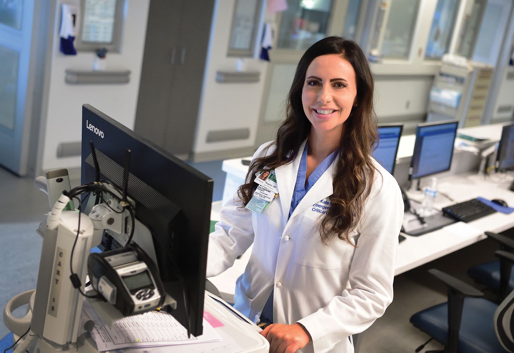 An image of ICU physician Kate Nugent smiling and working at her work station