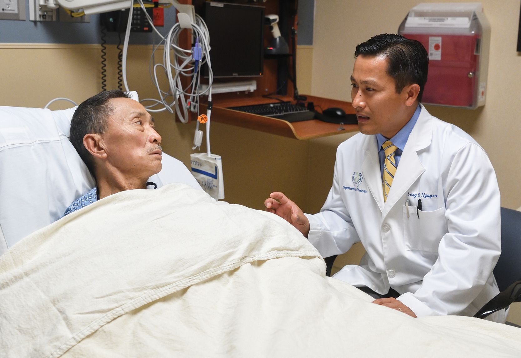 image of Dr. Long Nguyen talking with patient who is resting on a hospital bed
