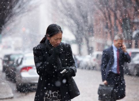 A woman coughing into her gloved hand while walking in the snow.
