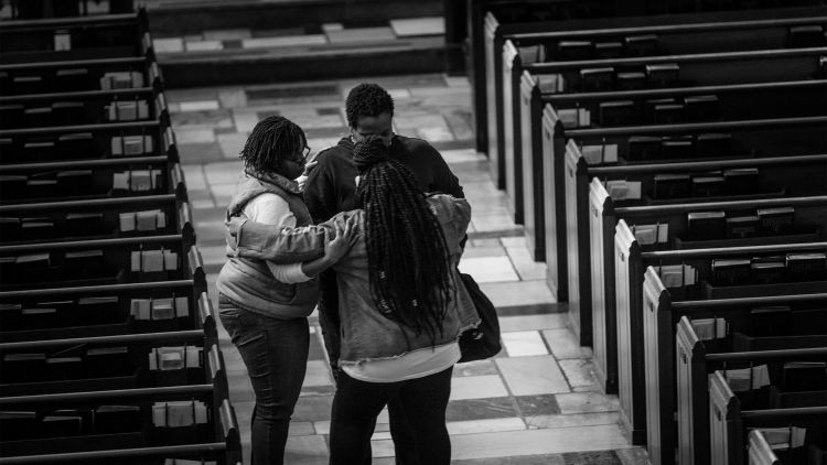 Three trip participants stand embracing each other in the church aisle.