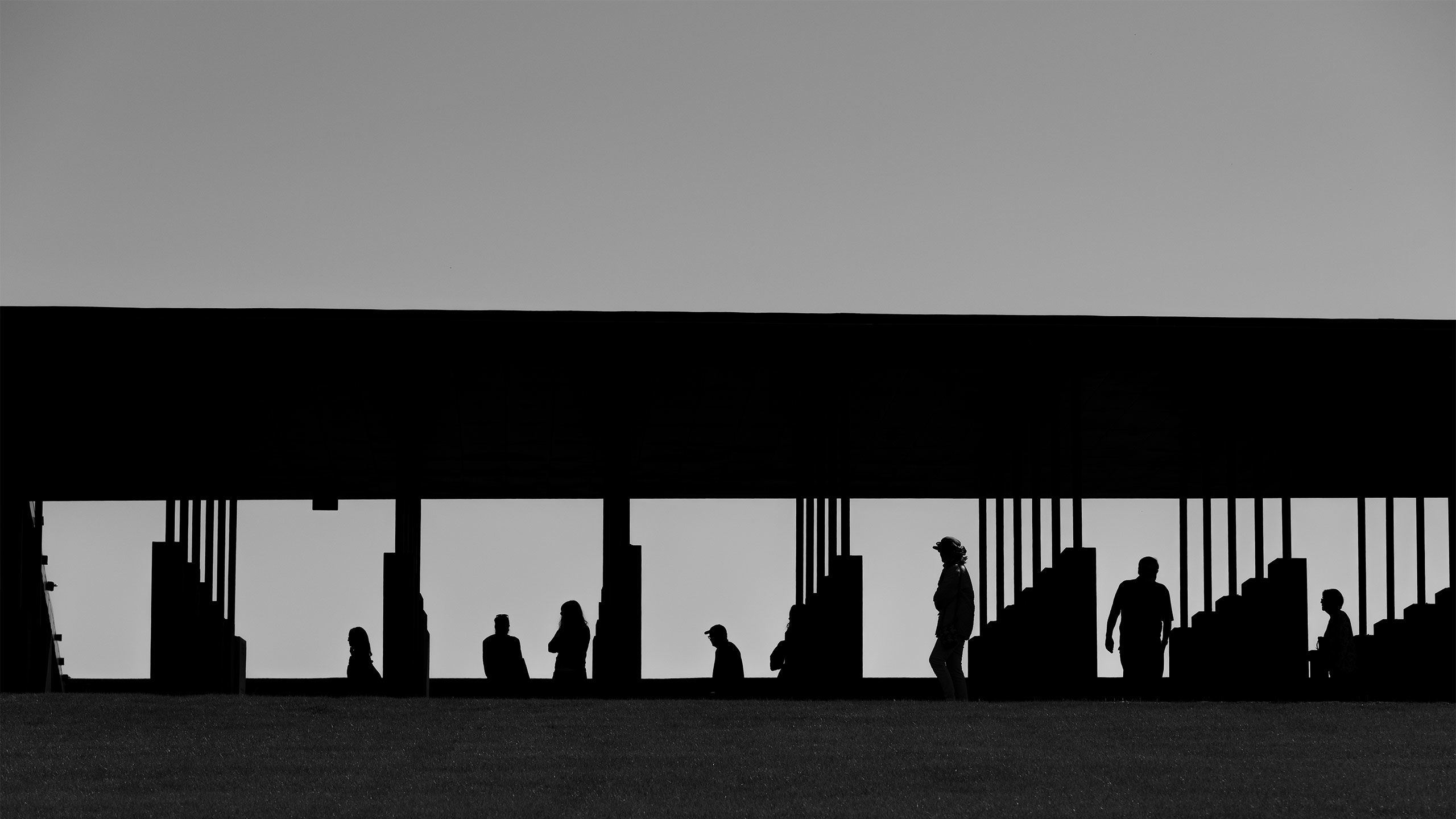 A photo taken from a distance shows people in silhouette visiting the National Memorial for Peace and Justice, standing among concrete columns.