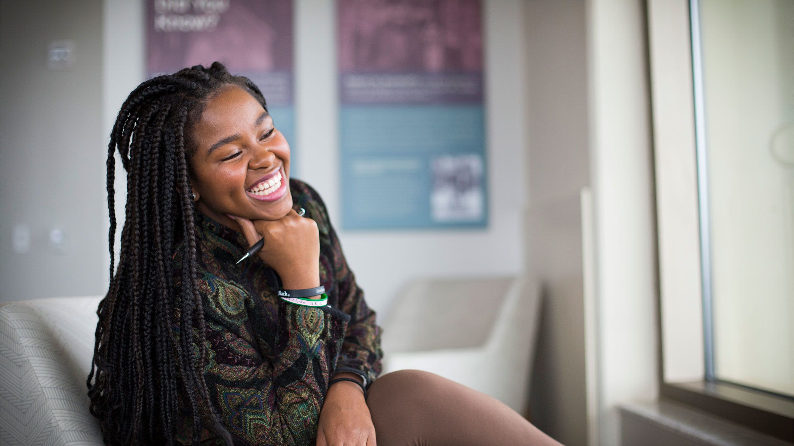 hristell Victoria Roach sits in a chair in the Rose Library, holding her pen and smiling.