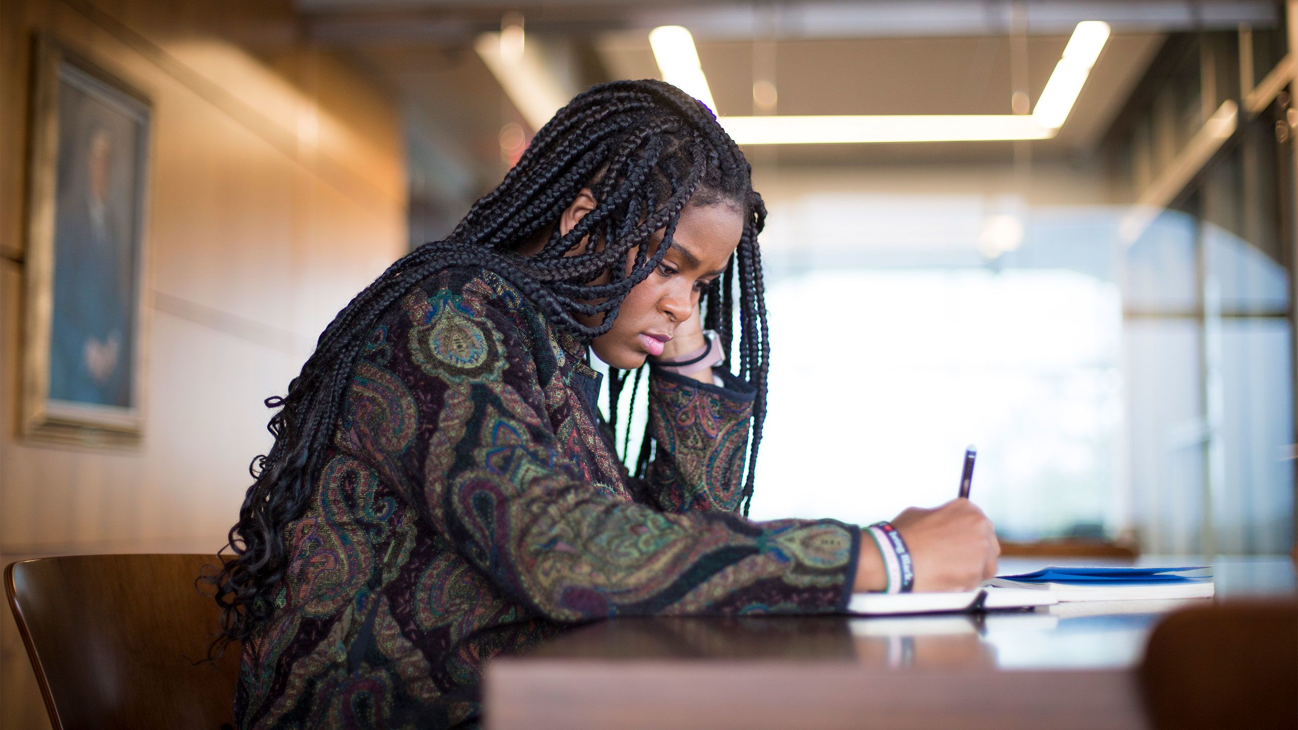 Christell Roach sits at a table in the Rose Library, writing witha  pen in her right  hand and with her head leaning on her left hand.