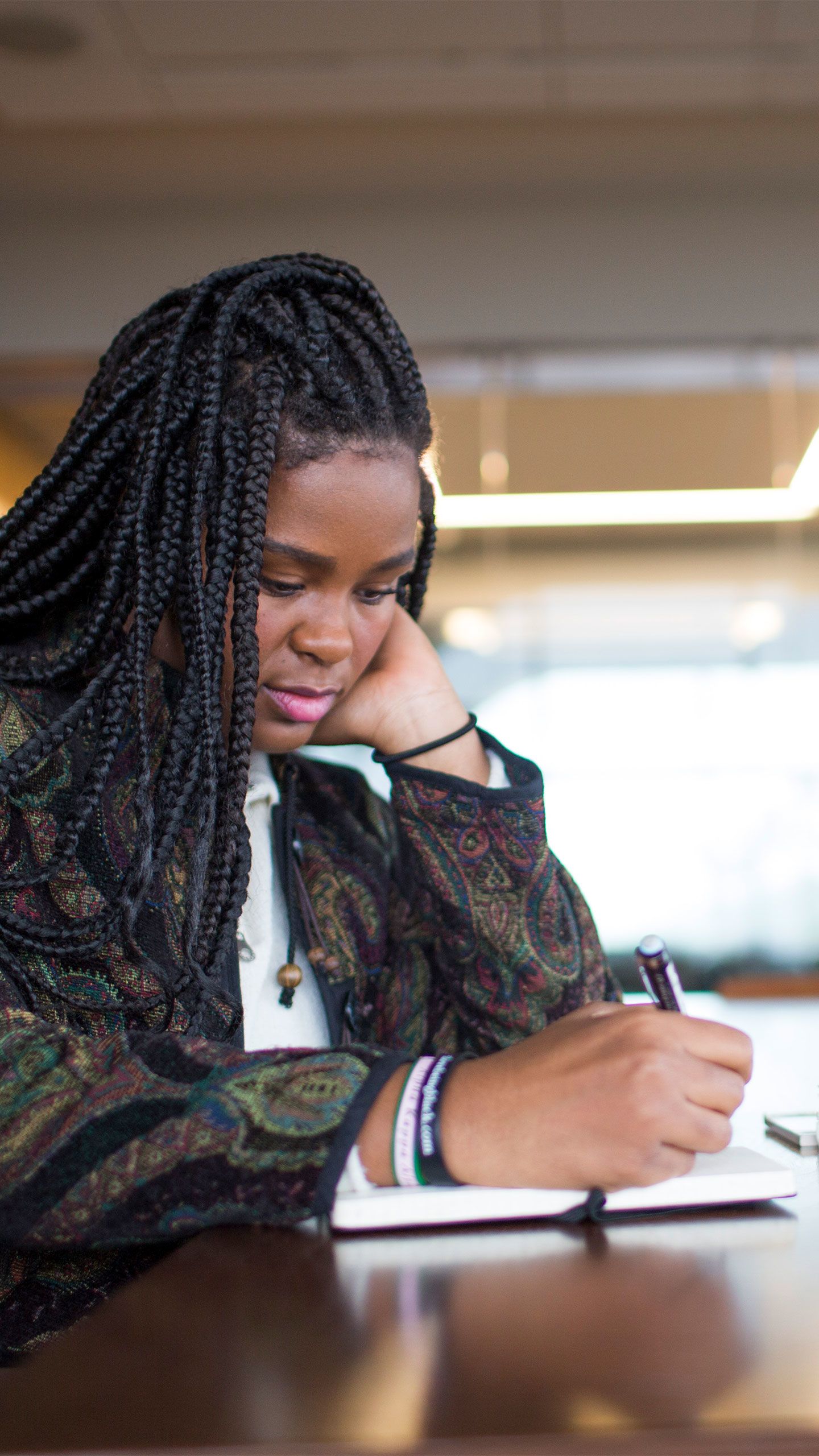 Christell Roach sits at a table in the Rose Library, writing witha  pen in her right  hand and with her head leaning on her left hand.