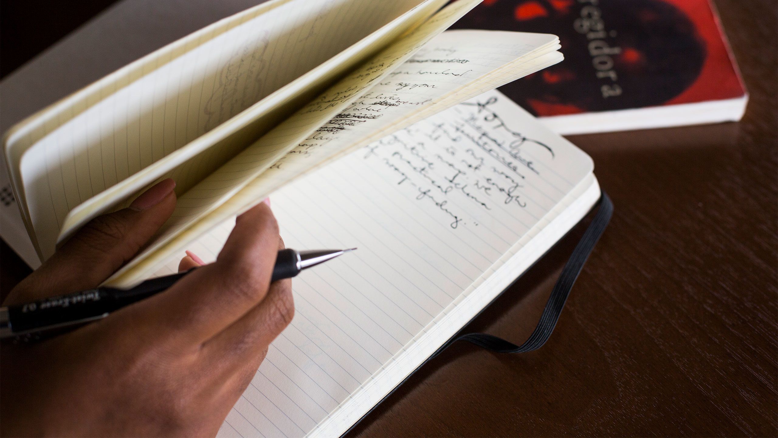 An up-close photo shows Christell Roach's hand holding a pencil and resting on an open notebook.