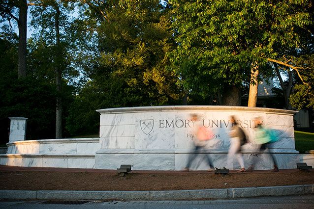 Three students walk hurriedly in front of the iconic marble Emory University sign