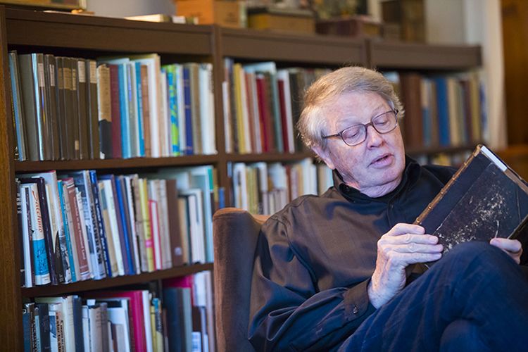 Burkett sits in a chair in the library of his home looking down at a book he is holding