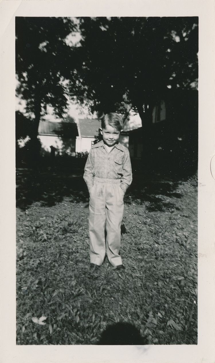 An old photograph of Burkett as a young boy standing in the grass with his hands in his pockets
