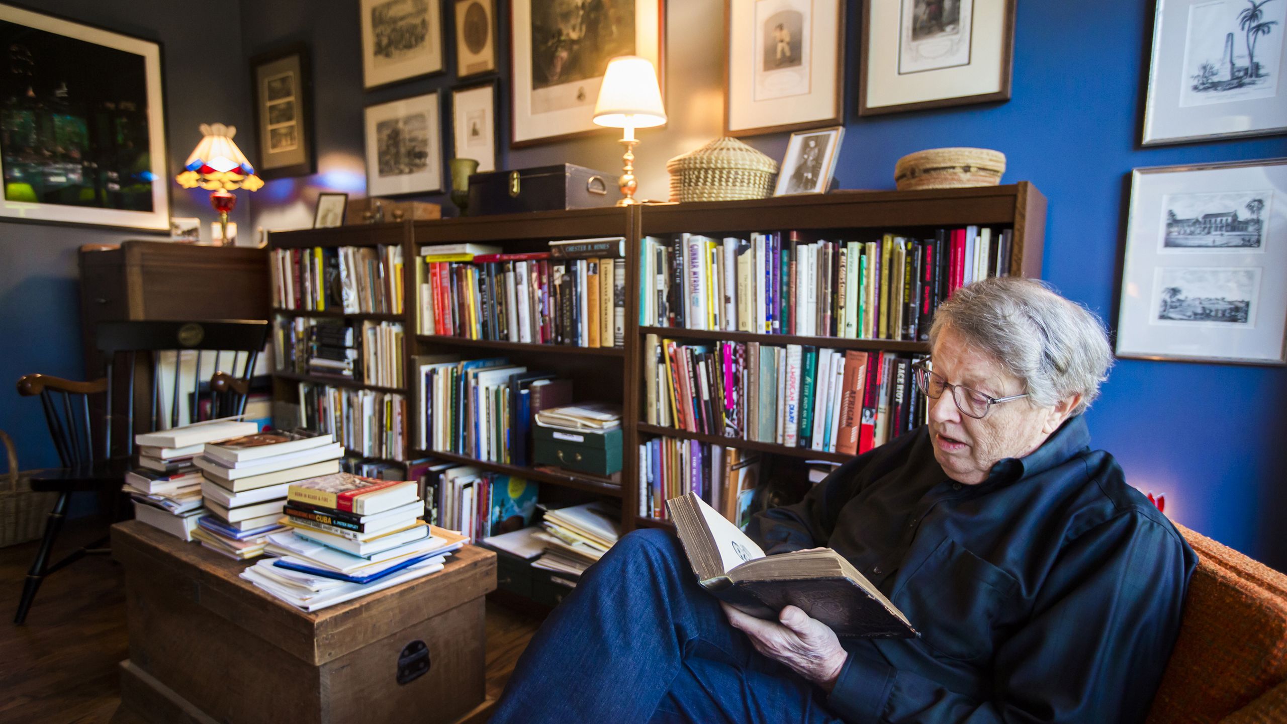 Burkett sitting in a chair in his home library while looking down at an open book in his hands