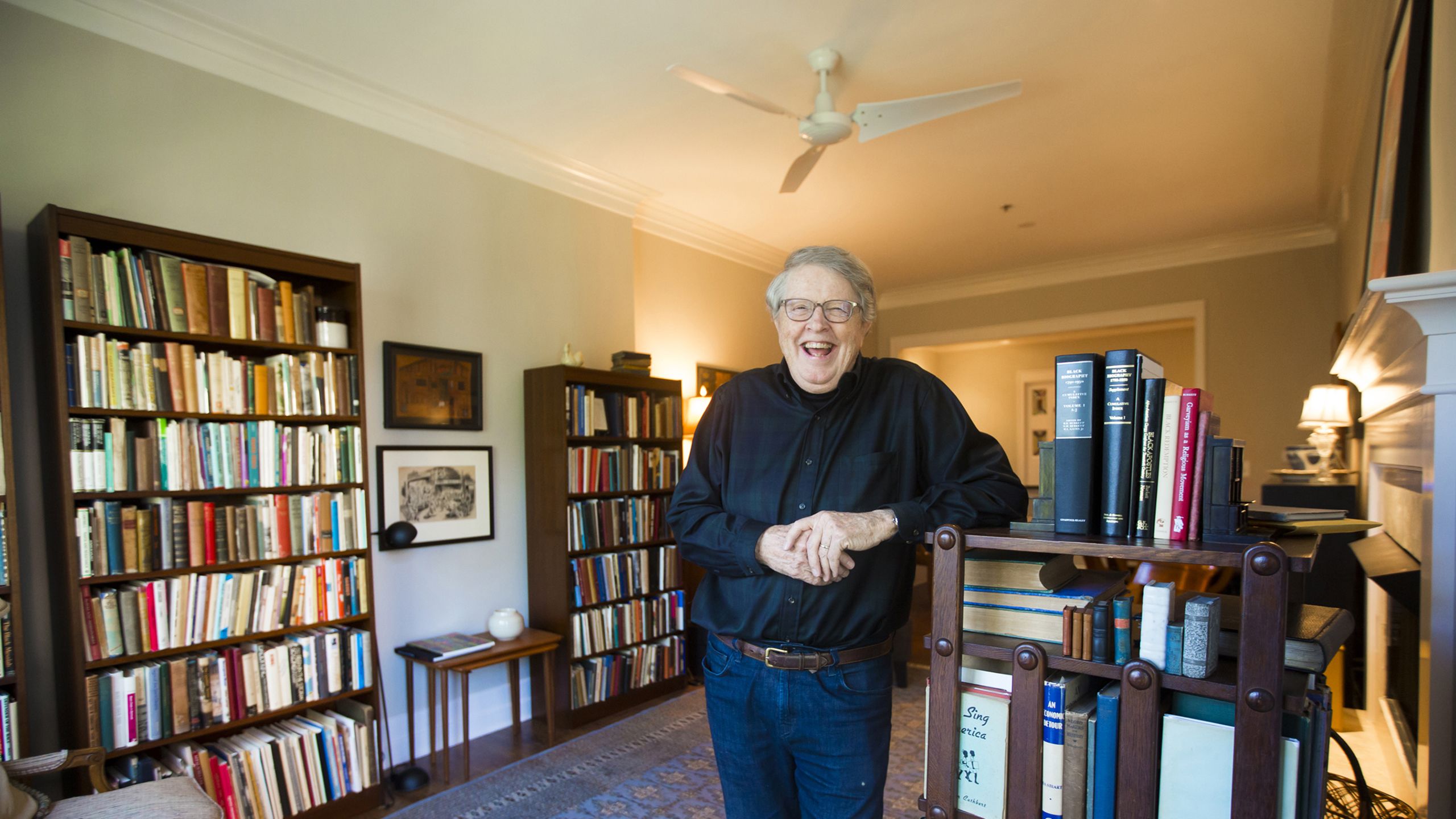 Burkett laughs while standing in the library of his home with his elbow resting on a turning bookcase