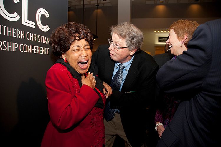 Dorothy Cotton laughing while Burkett leans in toward her from the right. Rosemary Magee is laughing with them.