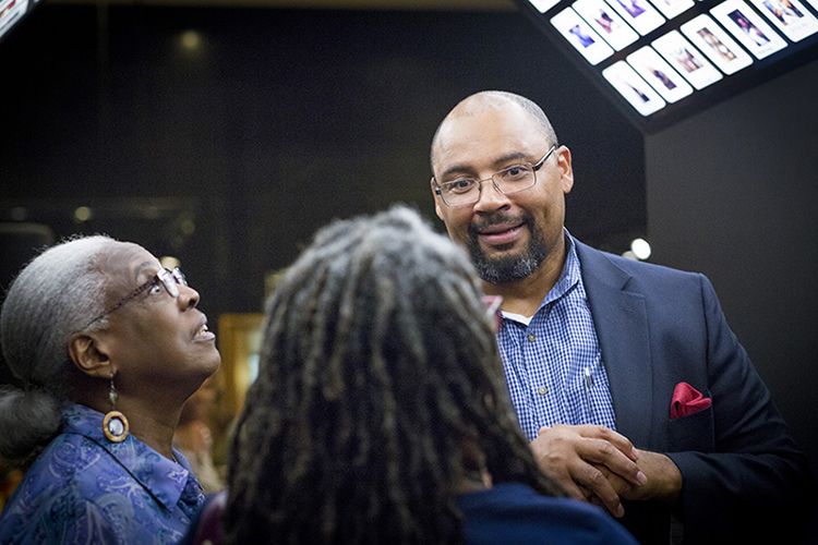 Pellom McDaniels smiles while standing next to two women looking at materials on display in the gallery