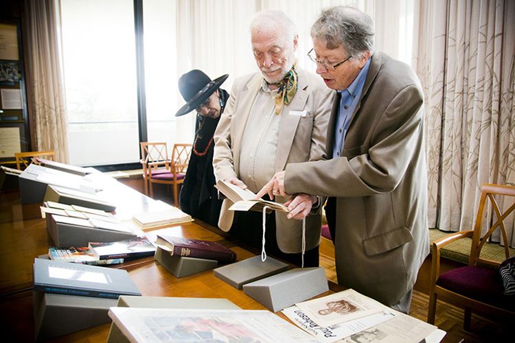 Camille Billops, James Hatch, and Burkett standing side by side looking at materials on a table in the archives