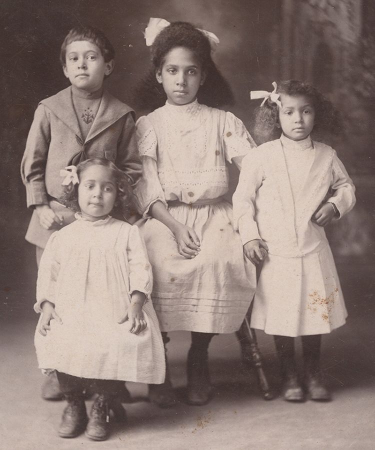 An old black and white photograph of four young children posing in their best clothes