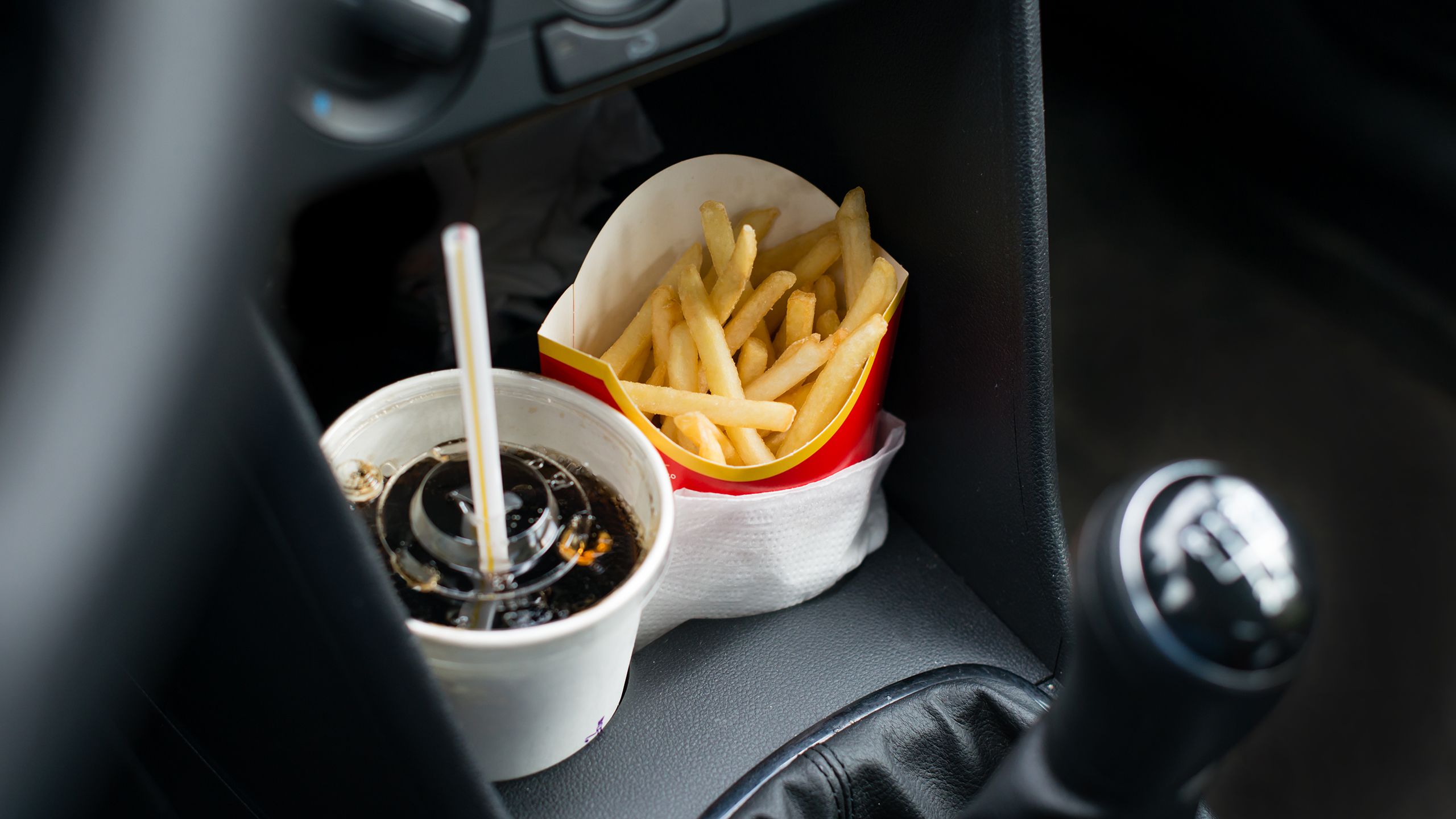 Fast food, including a soda and fries, in the console of a car.