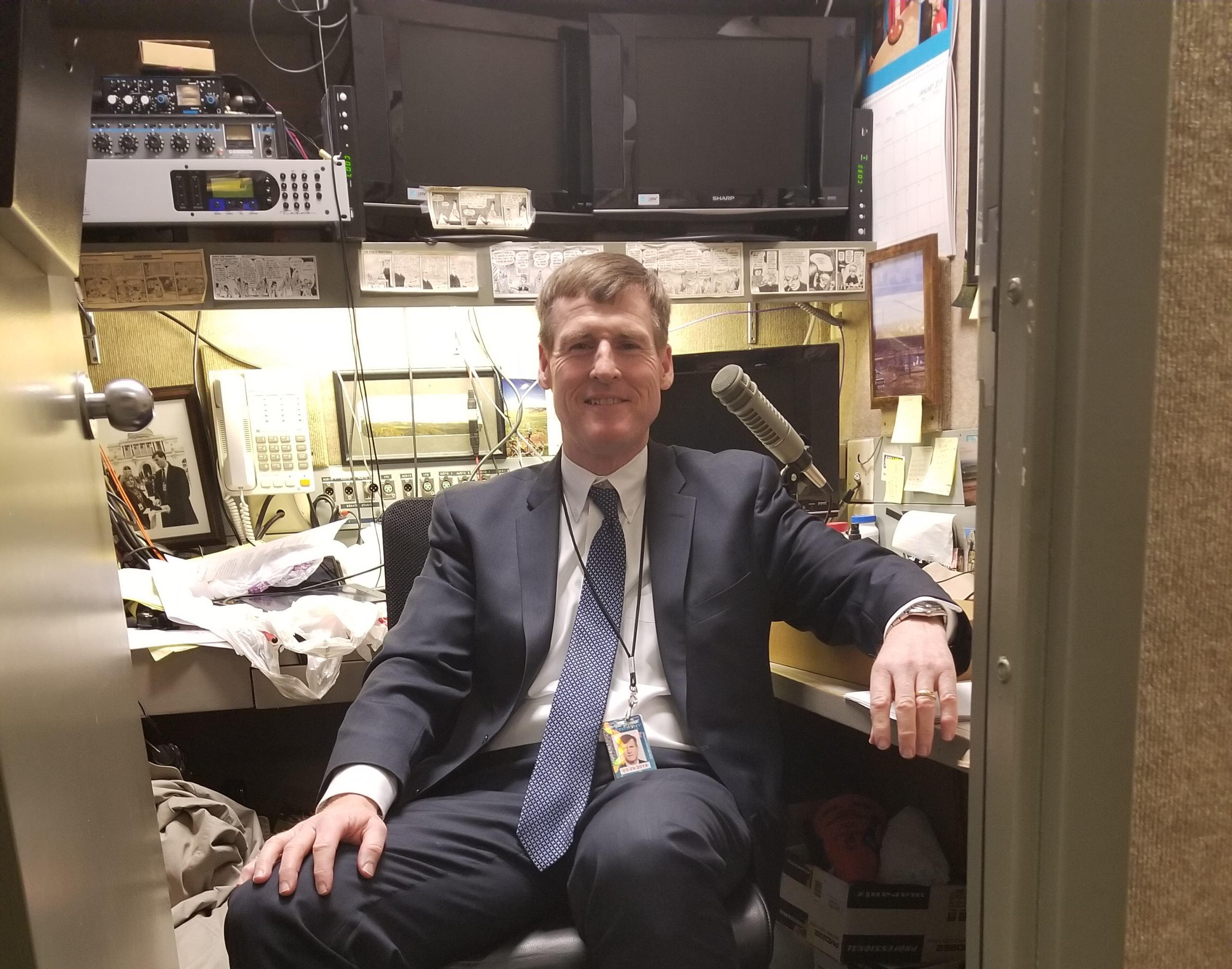 Jamie Dupree sits in his office surrounded by computers, papers, and microphones.