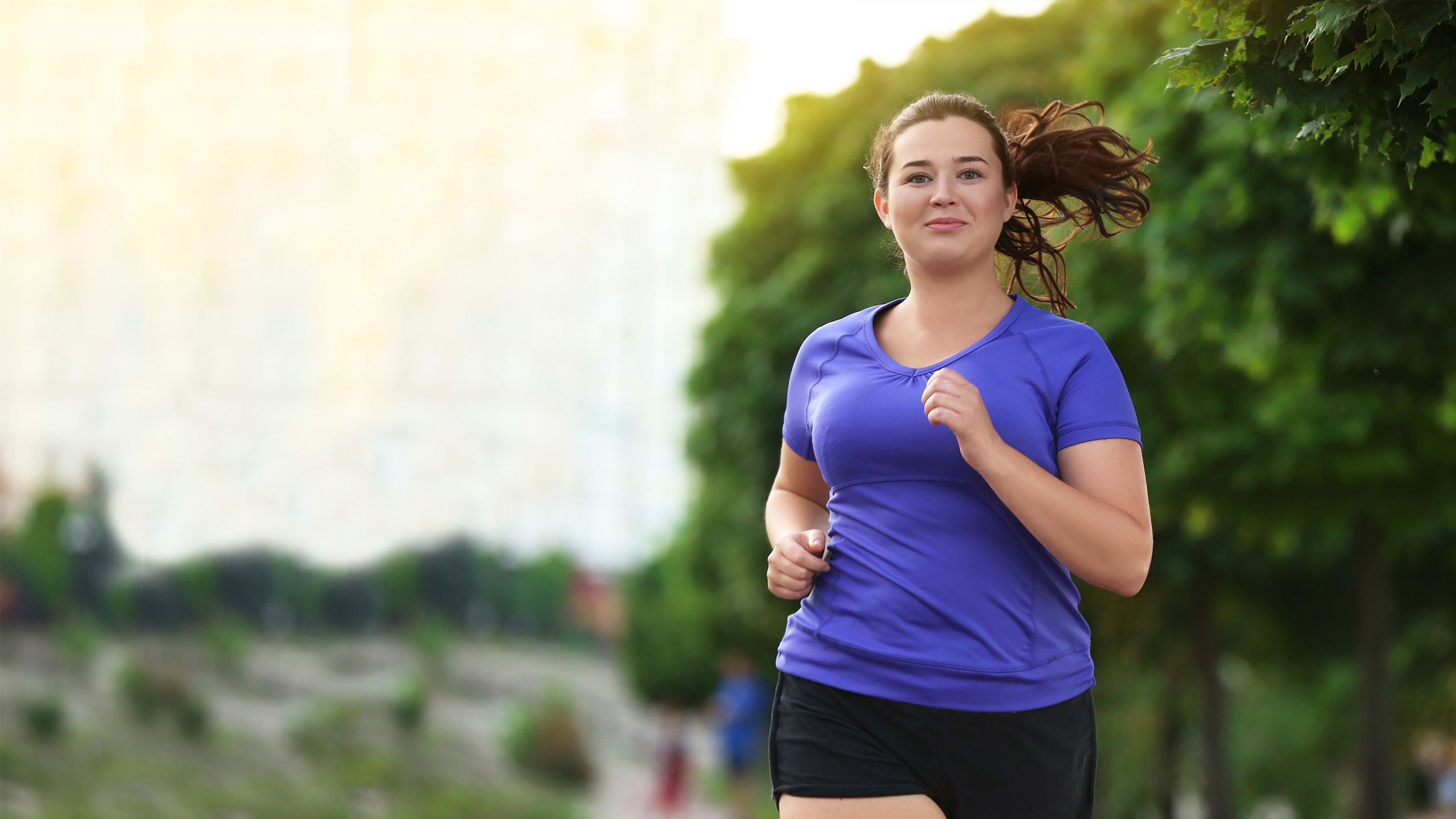 A woman jogging in sportswear along a tree-lined path.