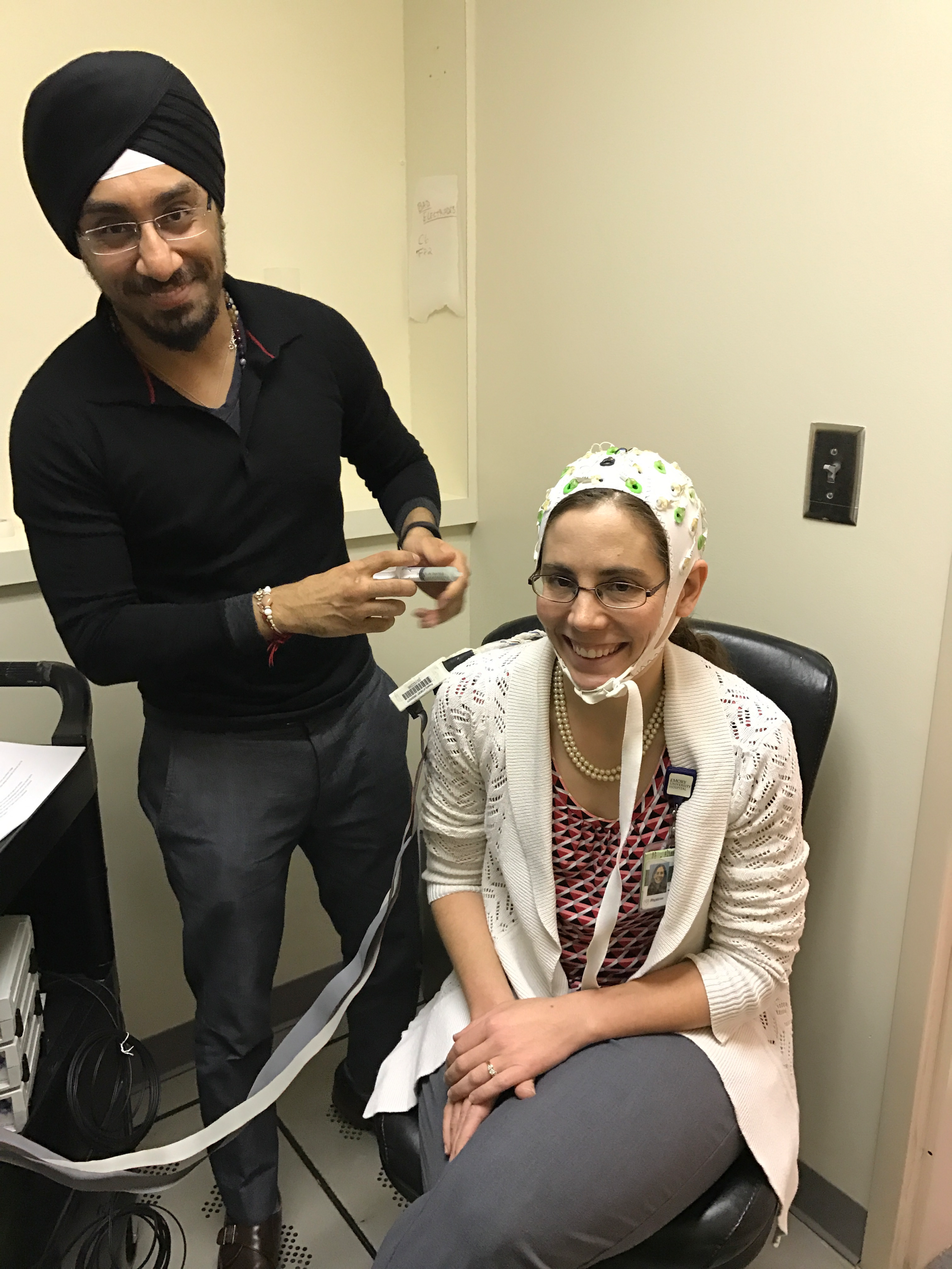A photo of neurologist Lynn Marie Trotti sitting down with a brain imaging cap on, and research associate Prabhjyot Saint preparing for a test run.