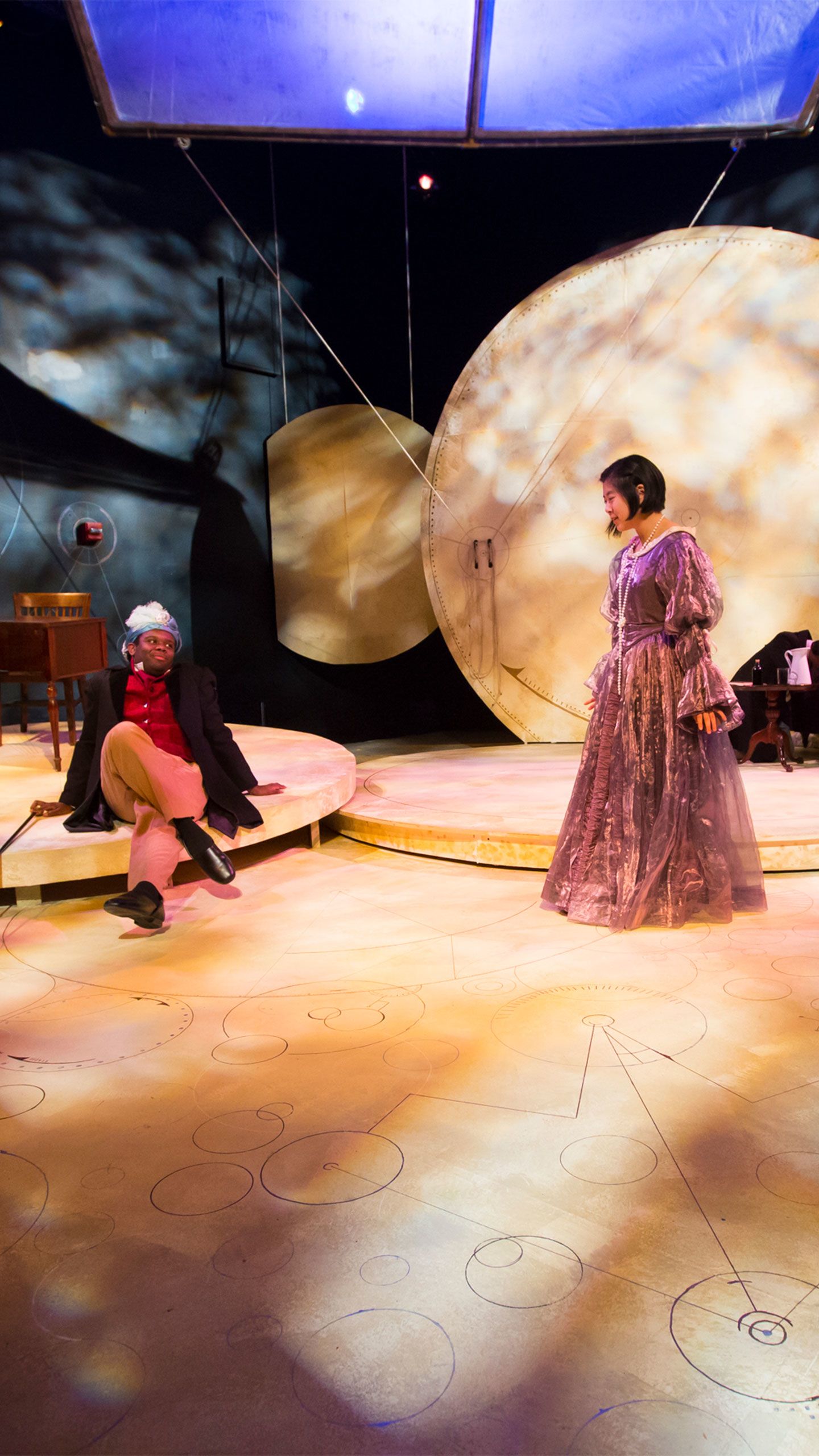 Two actors in 1800s period costumes stand on a stage at Oxford College.