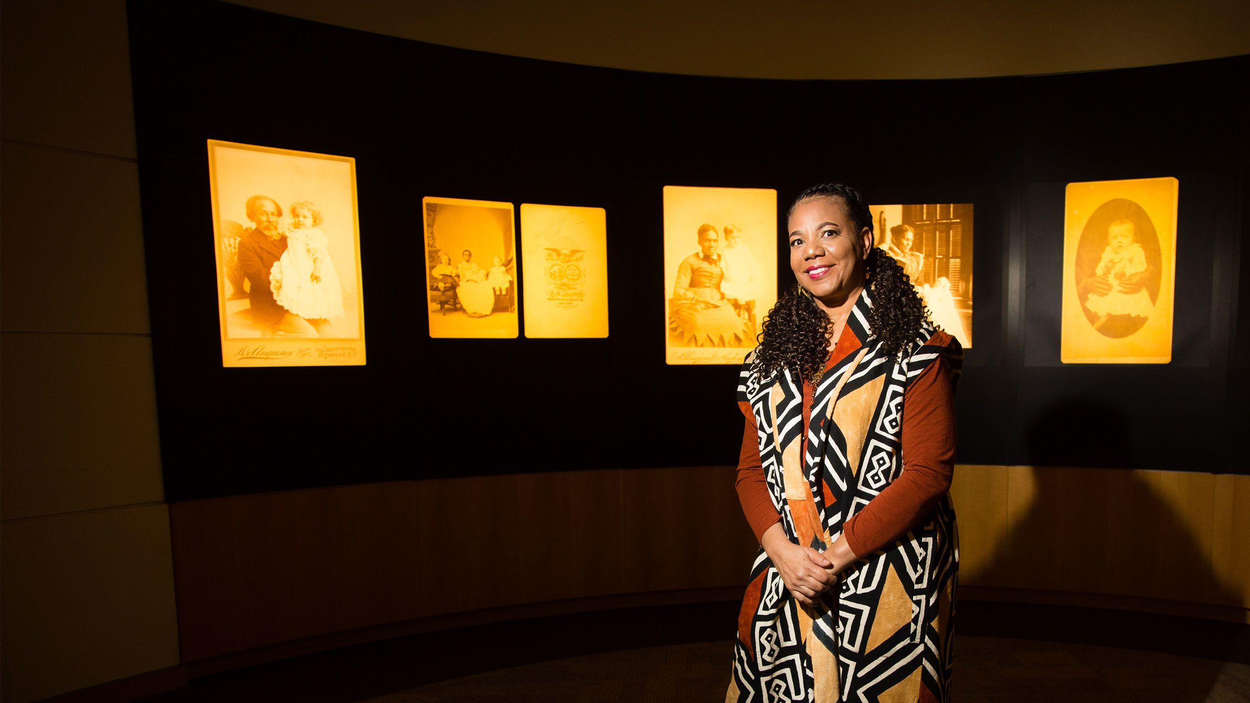 Emory professor Kimberly Wallace-Sanders stands in front of the Framing Shadows exhibit in Woodruff library. A series of sepia-toned historical photos show African American women holding white children.