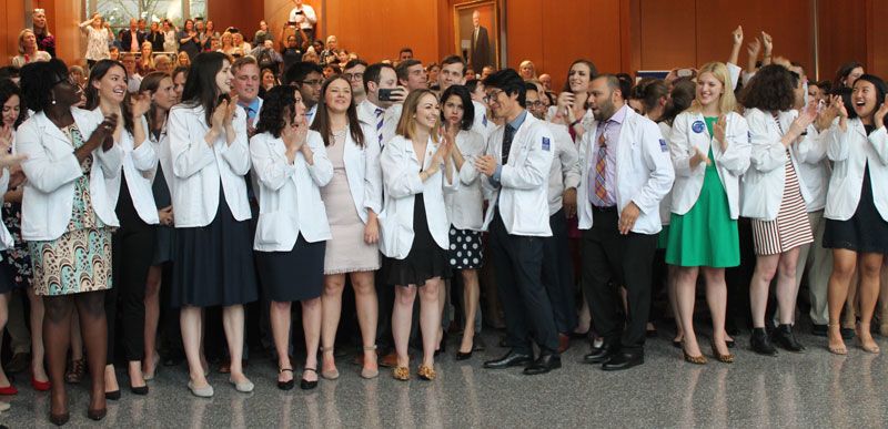 Emory medical students in white coats stand in a line waiting for the stroke of noon to rush forward and get the envelopes that will reveal where they matched for their residency training.