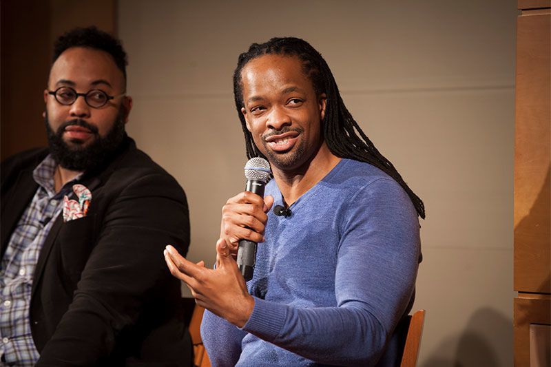 Jericho Brown holds a microphone as Kevin Young, seated next to him, looks on