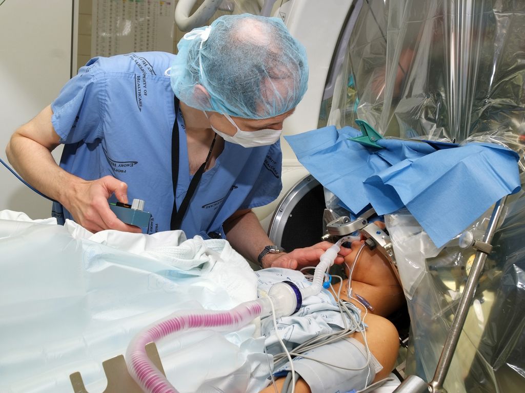 A patient on a surgical table covered by a tarp and a clinician monitoring them.