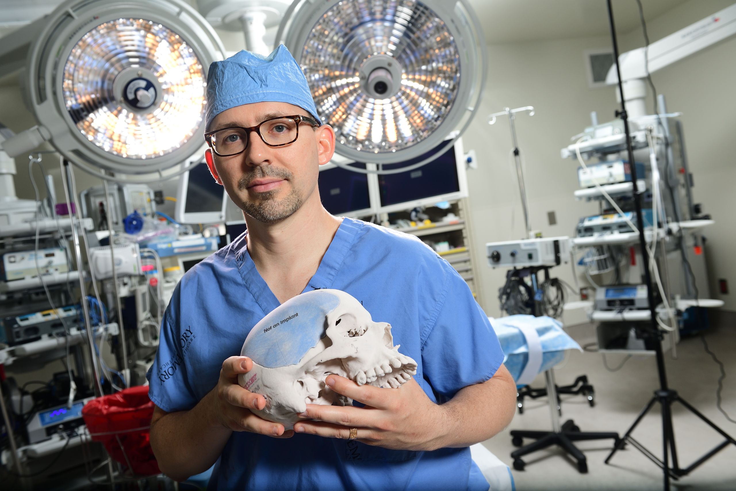 Dr. Jon Willie stands in an operating theater holding a model of a skull.
