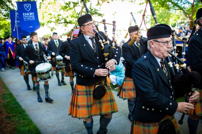 Drummers and bagpipe palyers walk in front of the Emory banner.