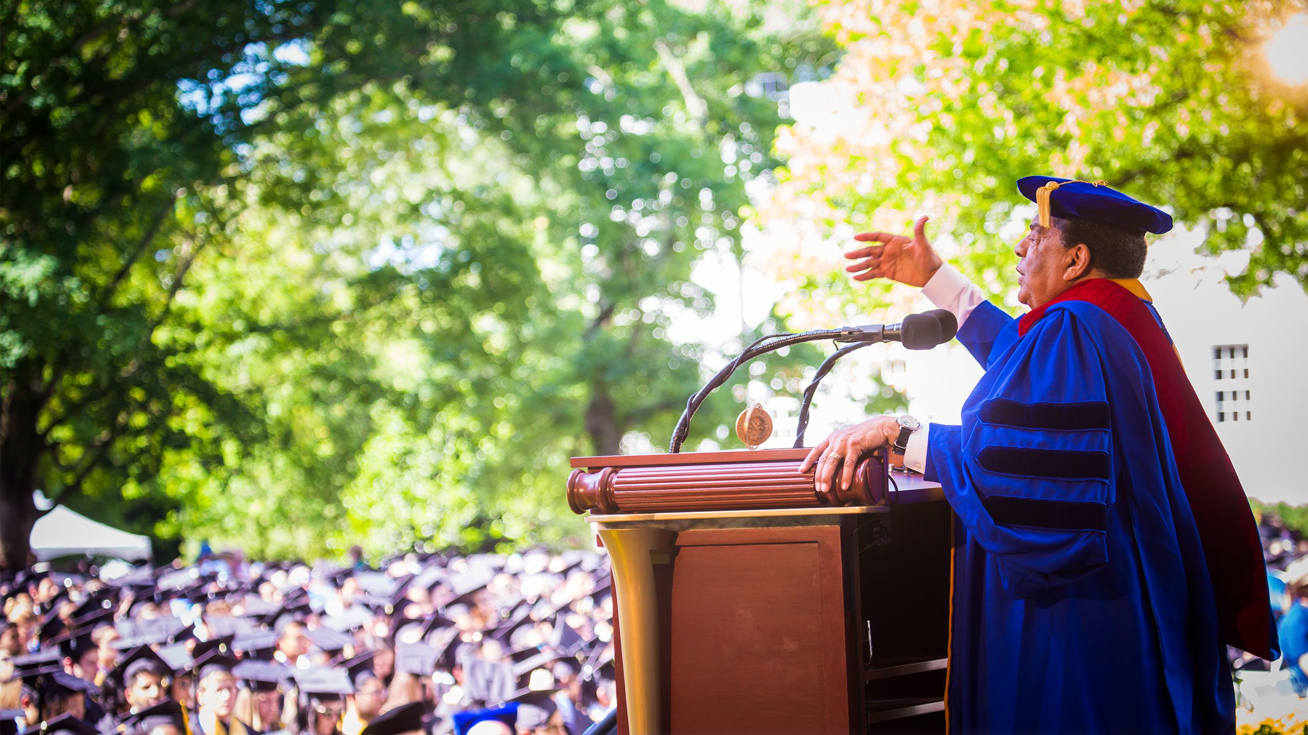 Andrew Young stand at the podium on the Commencement stage wearing a blue robe and gesturing as he speaks