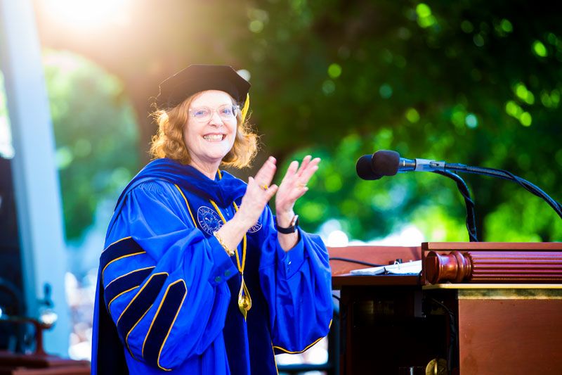 President Sterk, dressed in academic regalia, claps at the podium.