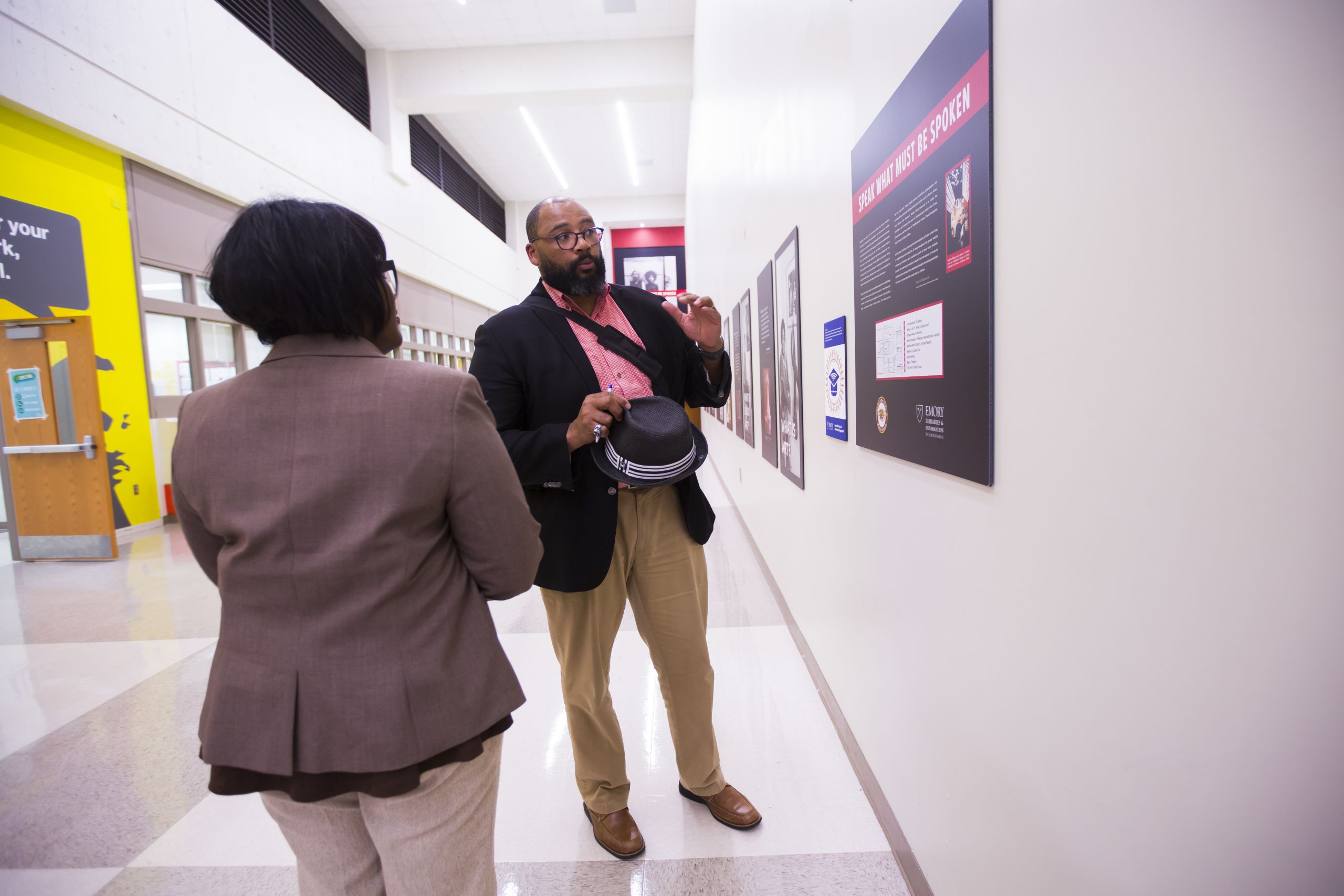 Pellom McDaniels stands in a hallway discussing posters on the wall highlighting African American artists.