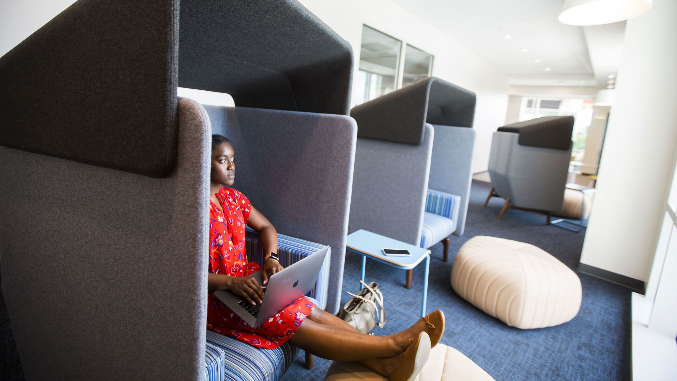 A young woman sits with her feet up in a privacy pod with her laptop