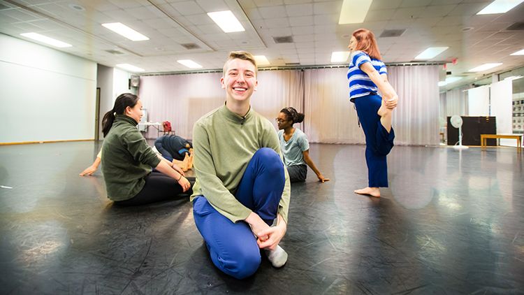 Laura Briggs smiling in a dance studio with dancers stretching in the background