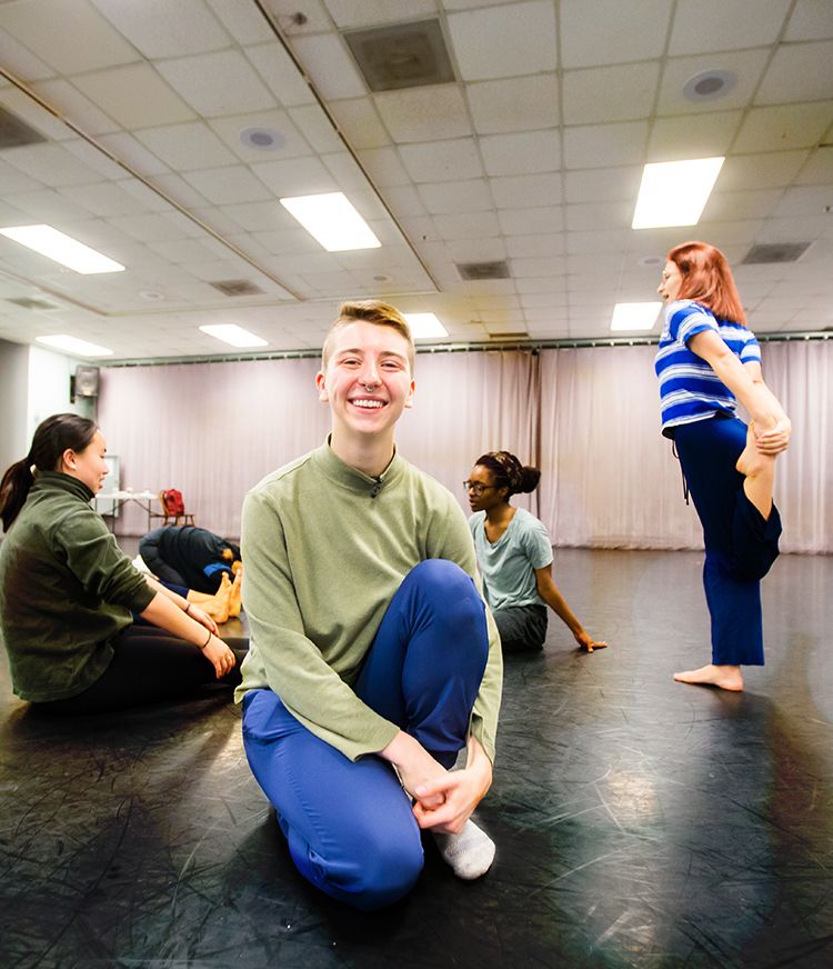 Laura Briggs smiling in a dance studio with dancers stretching in the background