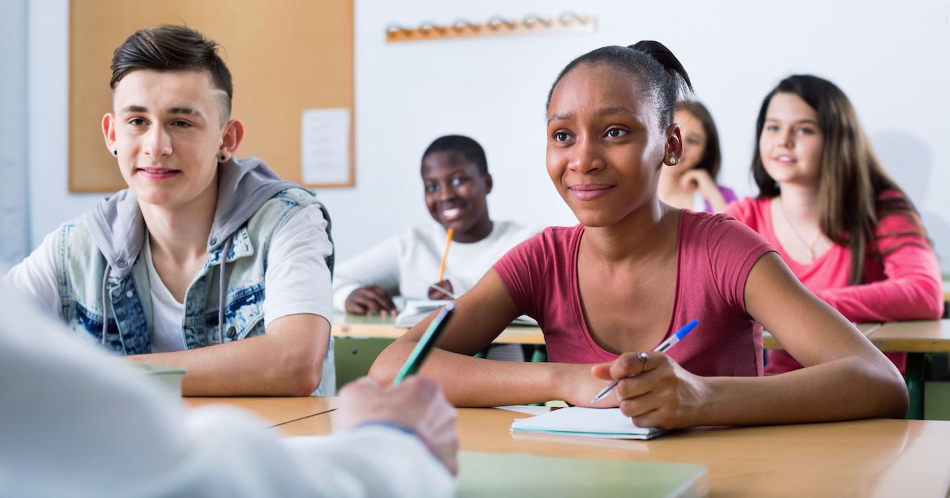 A classroom of middle-school students is seen listening and taking notes. 