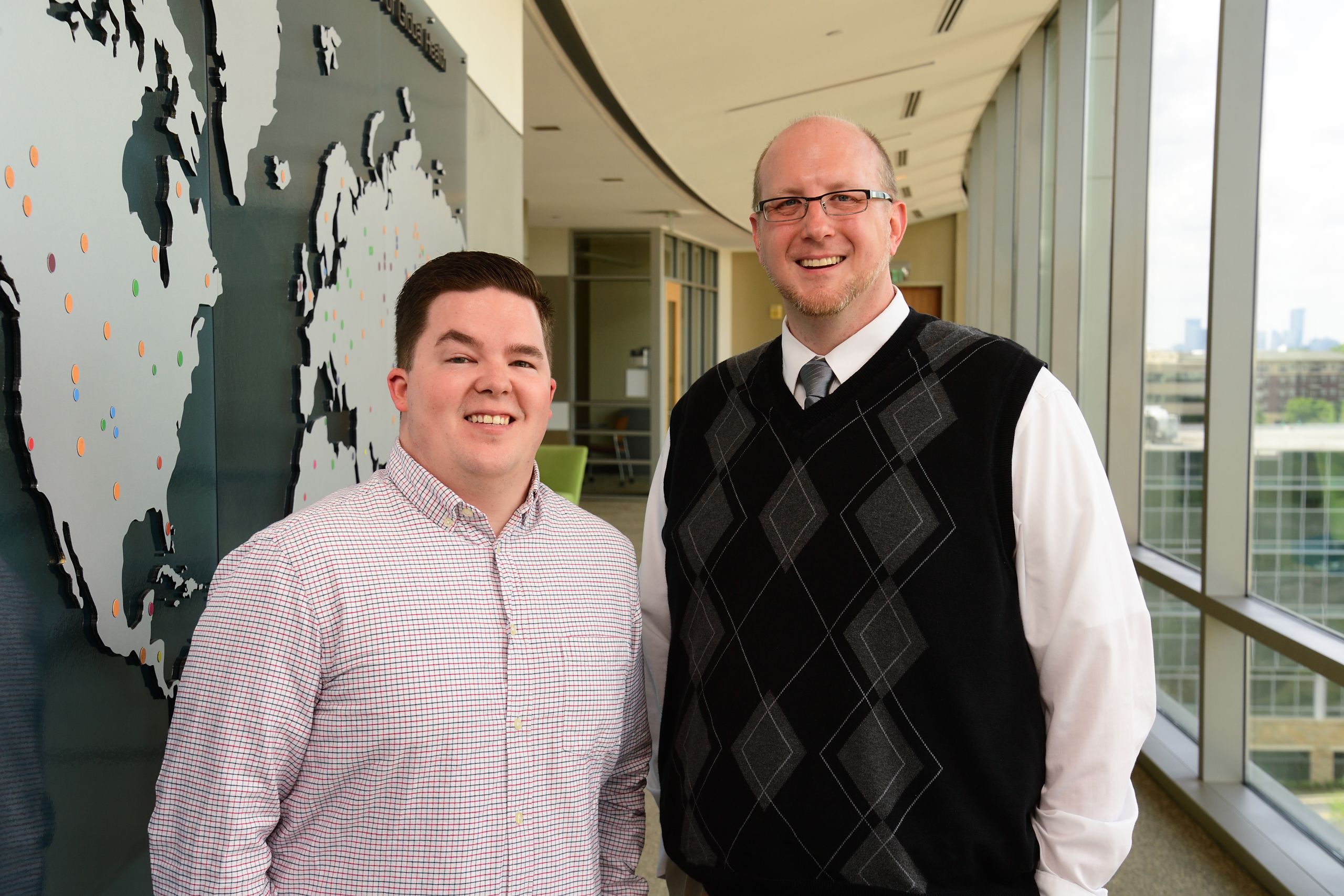 The two lead researchers are seen near a map of the world in Emory's Rollins School of Public Health.