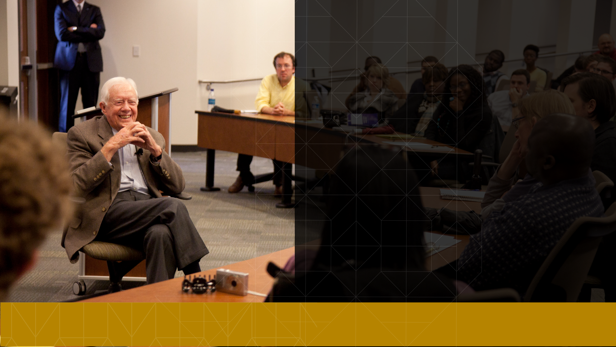 President Carter sits in a classroom and smiles at a group of students