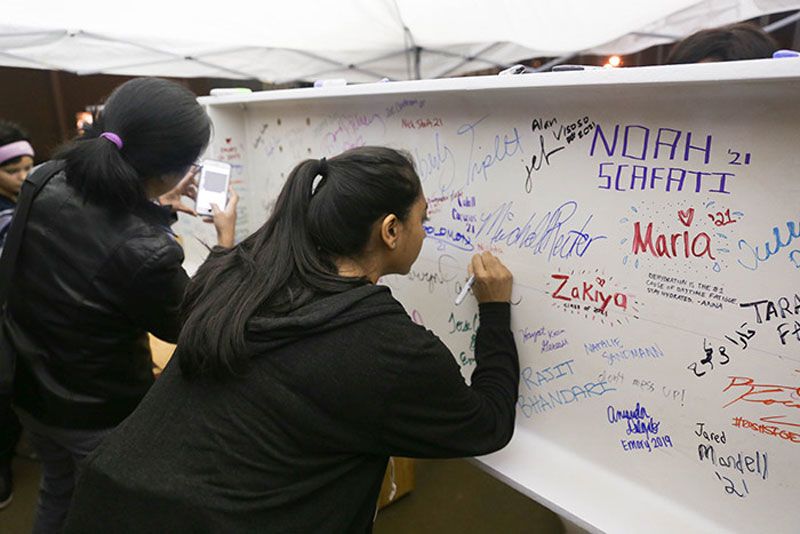 Students sign a white beam with colorful markers.