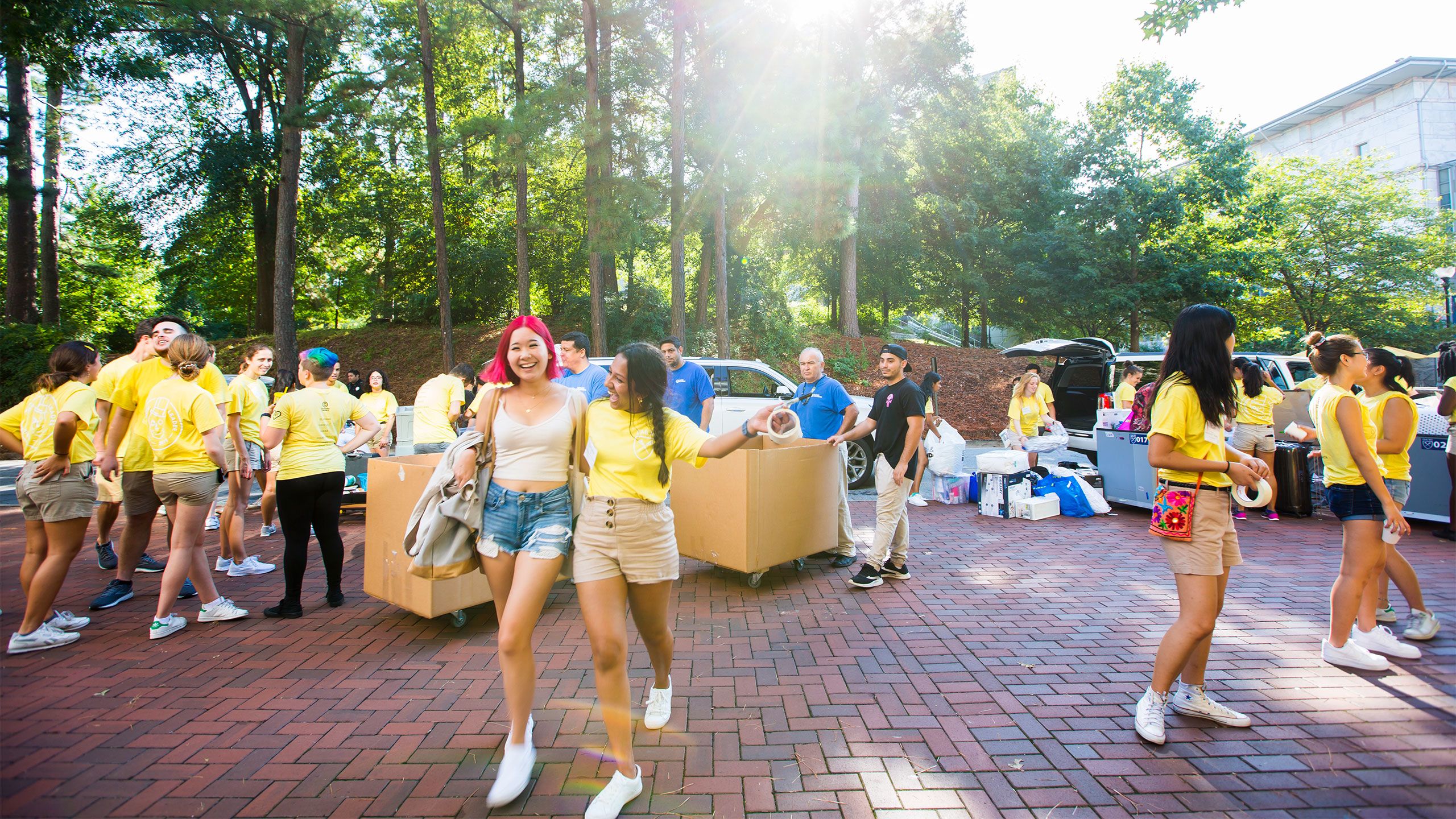 A student gets a hug from a student orientation leader as others leaders in yellow shirts help unload cars and move belongings