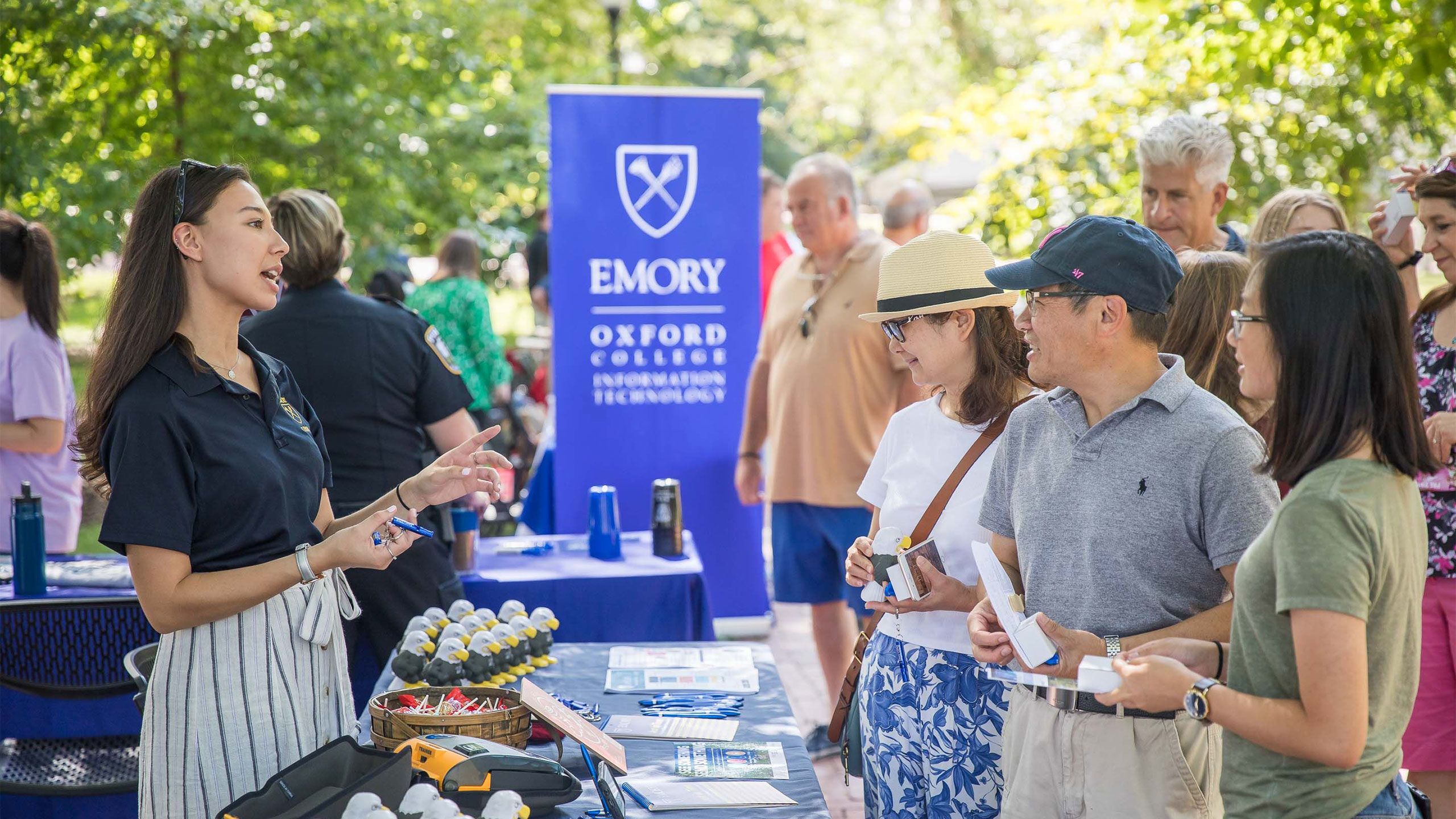 An Oxford staff member talks with parents at a table outdoors by an Emory banner