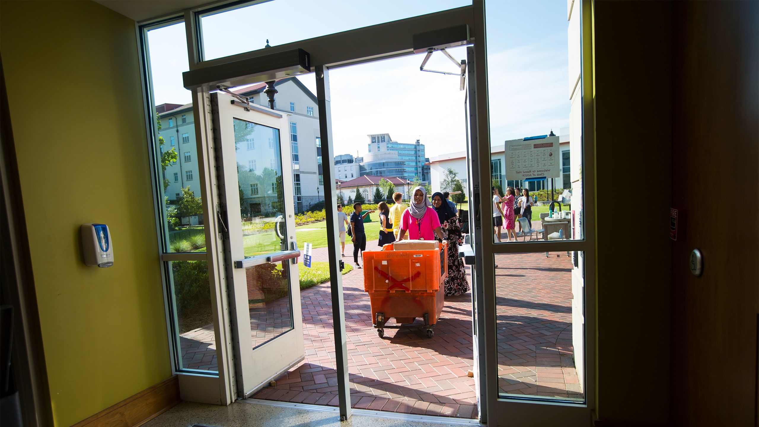 Student volunteers and families push a bin of belongings through a residence hall door