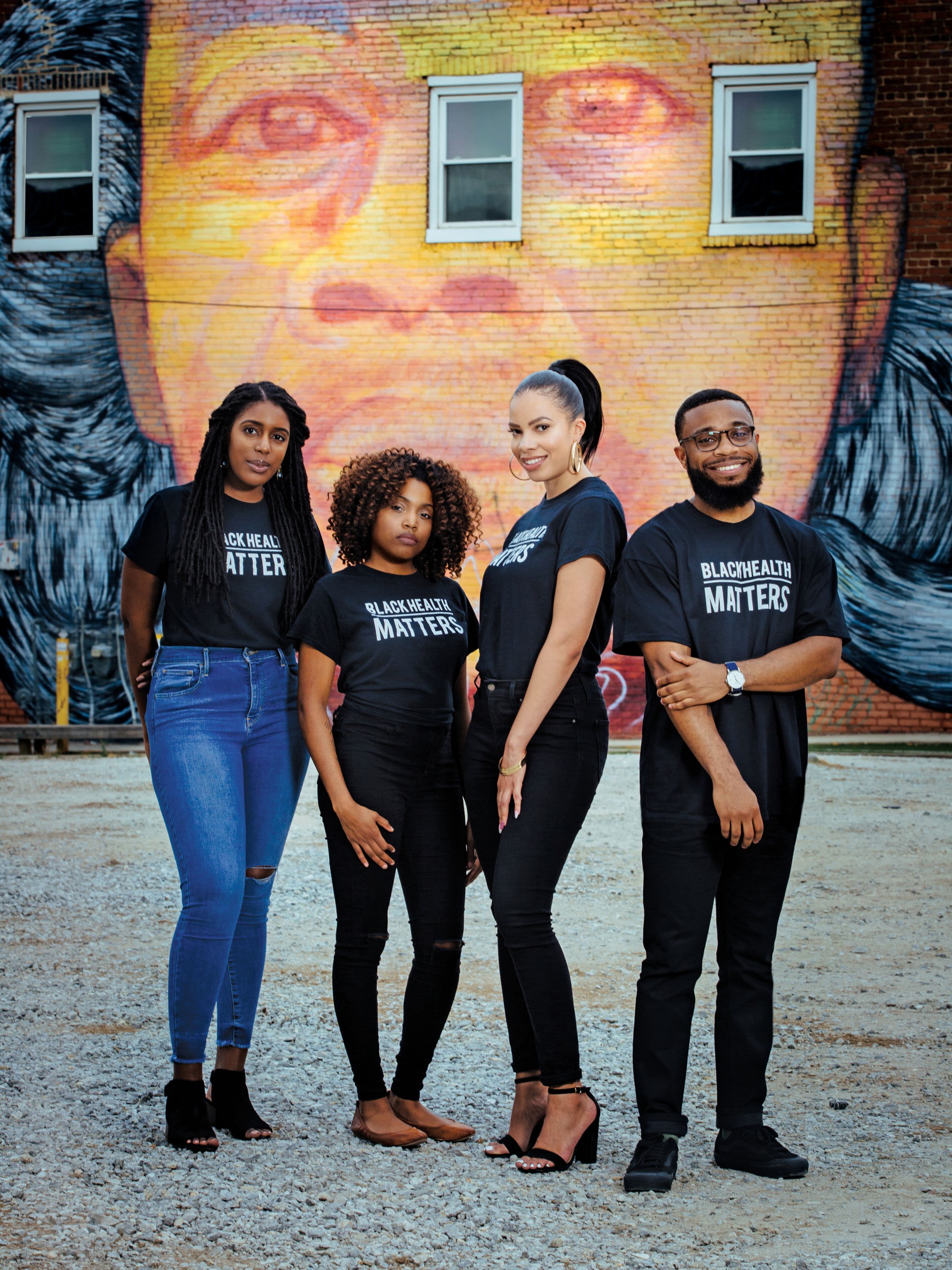 Paulah Wheeler, Khadijah Ameen, Mercilla Ryan-Harris, and Matthew McCurdy, all wearing T-shirts that say "Black Health Matters," pose in front of large mural on a building. The mural depicts an African American man's face.