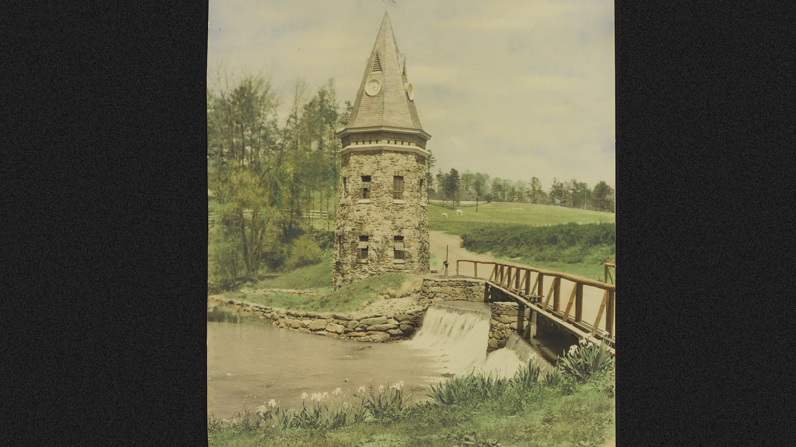 bridge and water fall in foreground water tower and field in background
