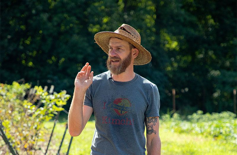 Wearing a straw hat and t-shirt, Joe Reynolds stands in one of the fields he farms.