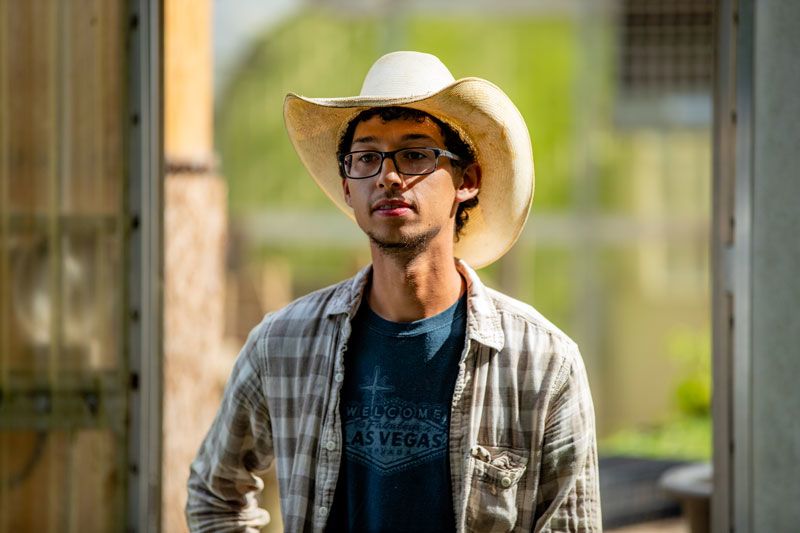 Demetrius Milling, wearing a cowboy hat and plaid shirt, photographed on the farm where he works