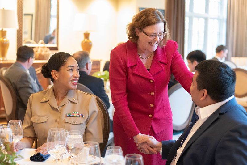 Emory President Claire Sterk shakes hands with a man seated at a table as a woman in a military uniform looks on.