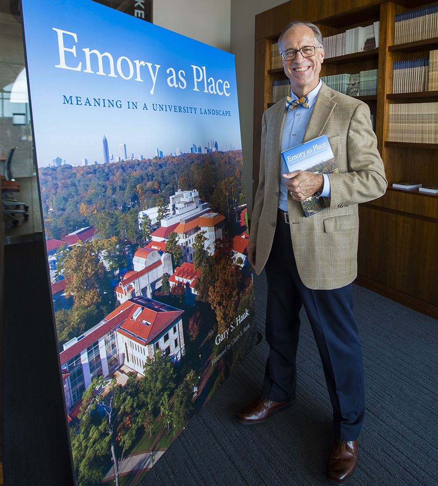 Hauk posing alongside a large poster showing the front cover of his book, "Emory as Place"