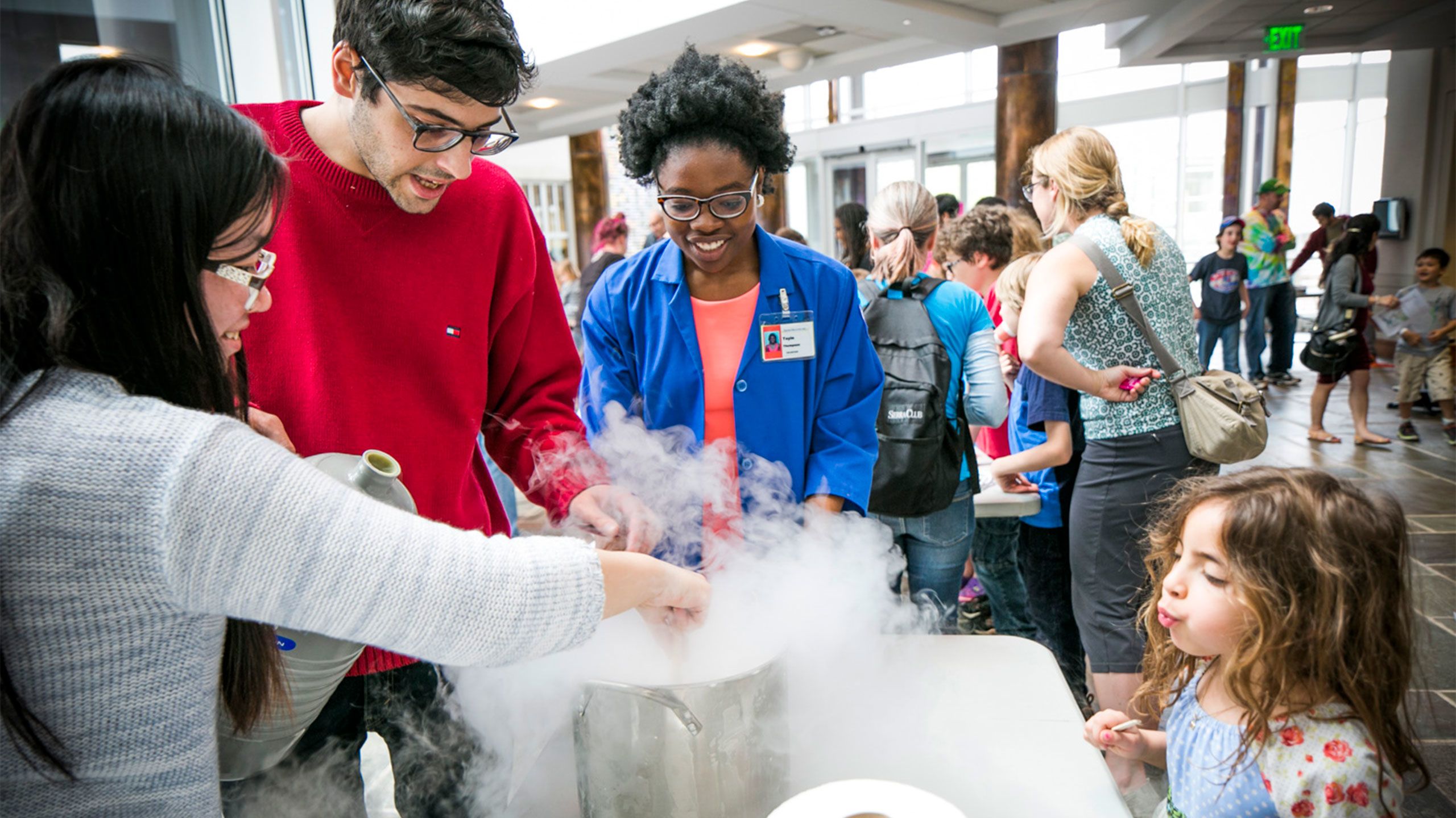 A child watches in wonder as three Emory stduents conduct an experiment. More people are visible at other demontrations in the background.