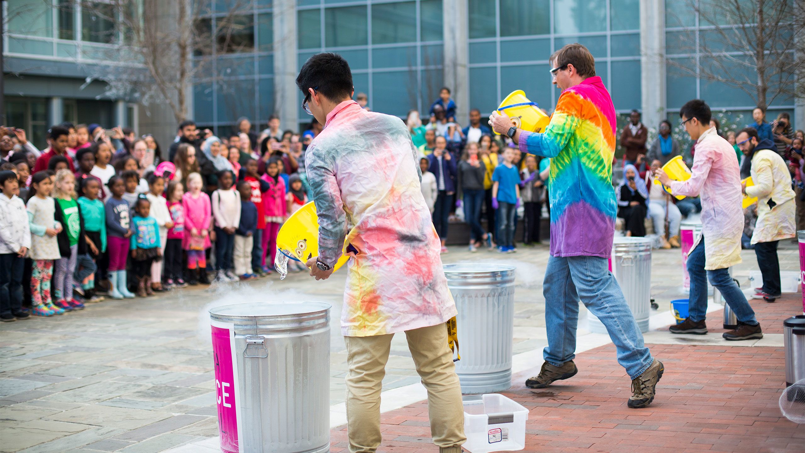 With a crowd of children and adults watching, Emory scientists with tie-dye lab coats prepare to dump buckets into trash cans at the Atanta Science Festival on campus.